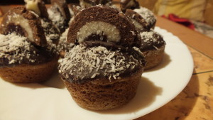 kokosové muffinky - zdobené čokoládovou polevou, kokosem a navrchu je ještě půlkolečko kokosové rolády